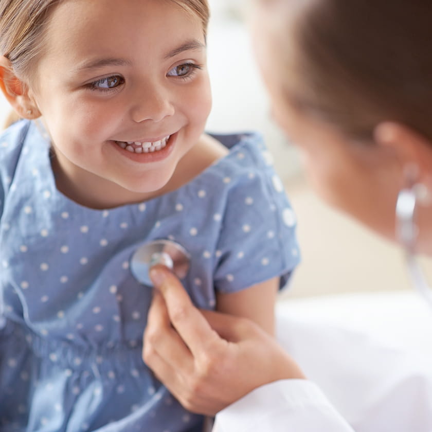 Smiling young girl with a doctor using a stethoscope on her